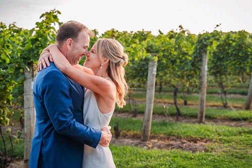 bride and groom embracing in front of vineyards at Honsberger Estate Winery