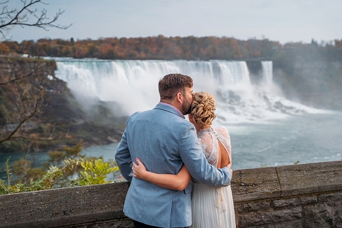  groom kissing bride while they look at Niagara Falls