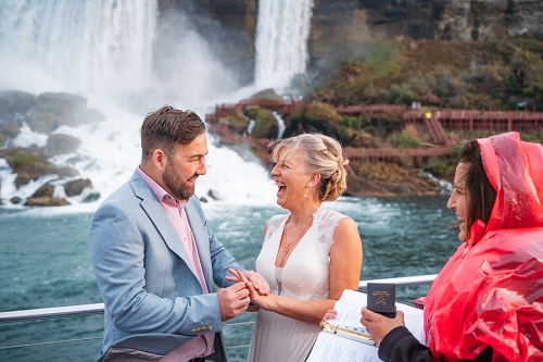 groom putting ring on brides finger with niagara falls in background