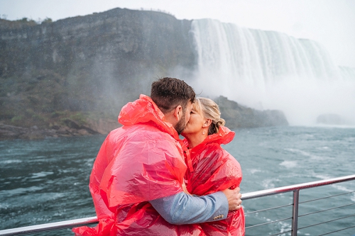  couple kissing on hornblower cruise wearing ponchos with niagara falls in background