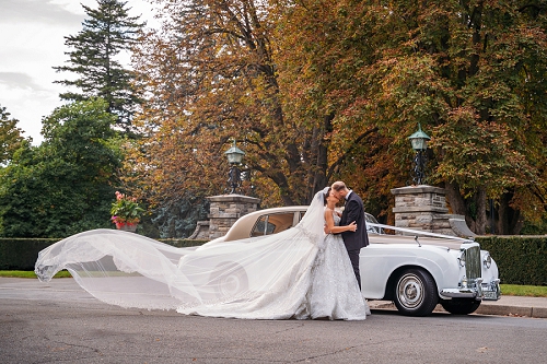 stunning bride with long veil kissing groom in front of vintage Bentley at white oaks resort